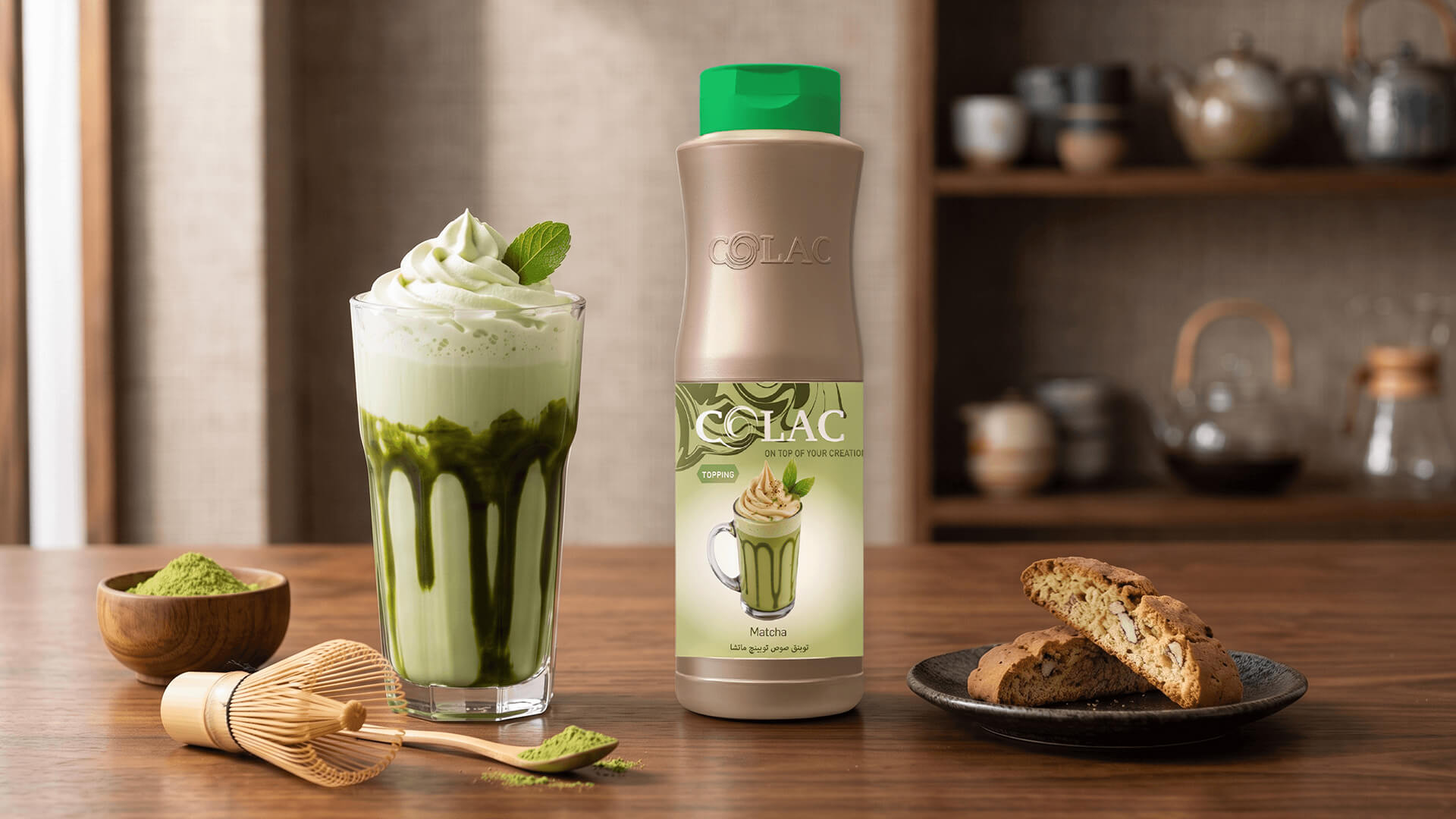 Botella de sirope Colac Topping sabor Matcha junto a un vaso de matcha latte helado con crema batida, polvo de té verde y galletas biscotti sobre una mesa de madera.